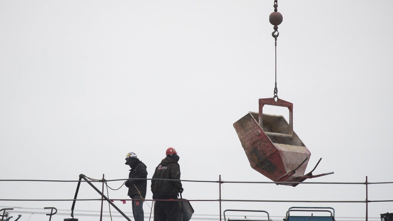 Des travailleurs de la construction sur un toit avec une grue près d'eux.