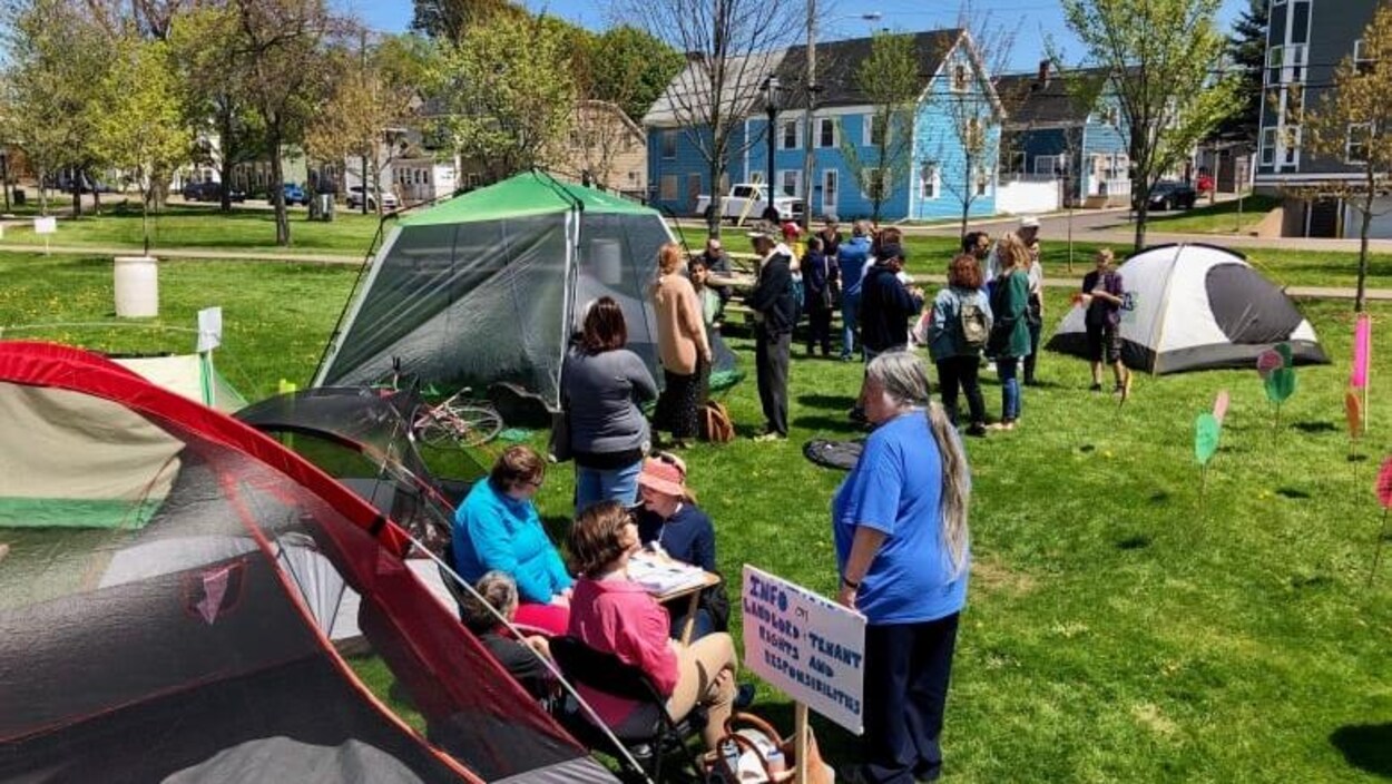 des tentes plantées dans un parc à l'été et avec des citoyens qui discutent