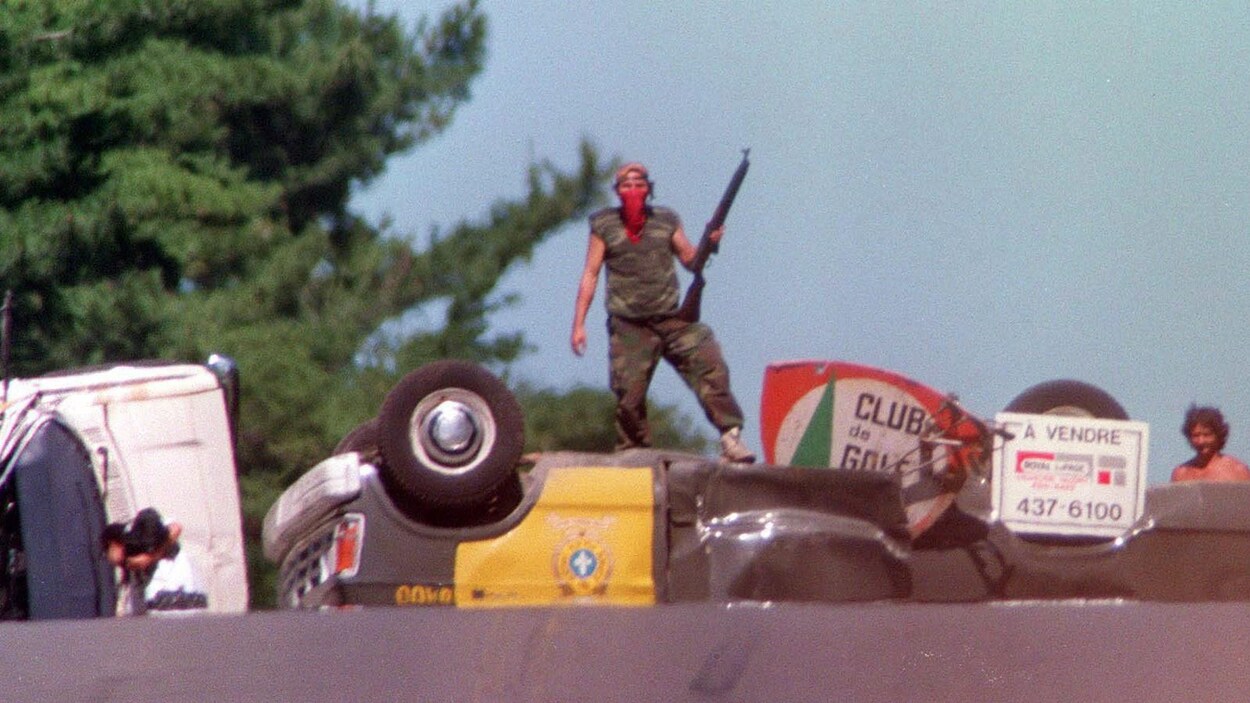 Un Mohawk se tient debout sur une voiture de police renversée.