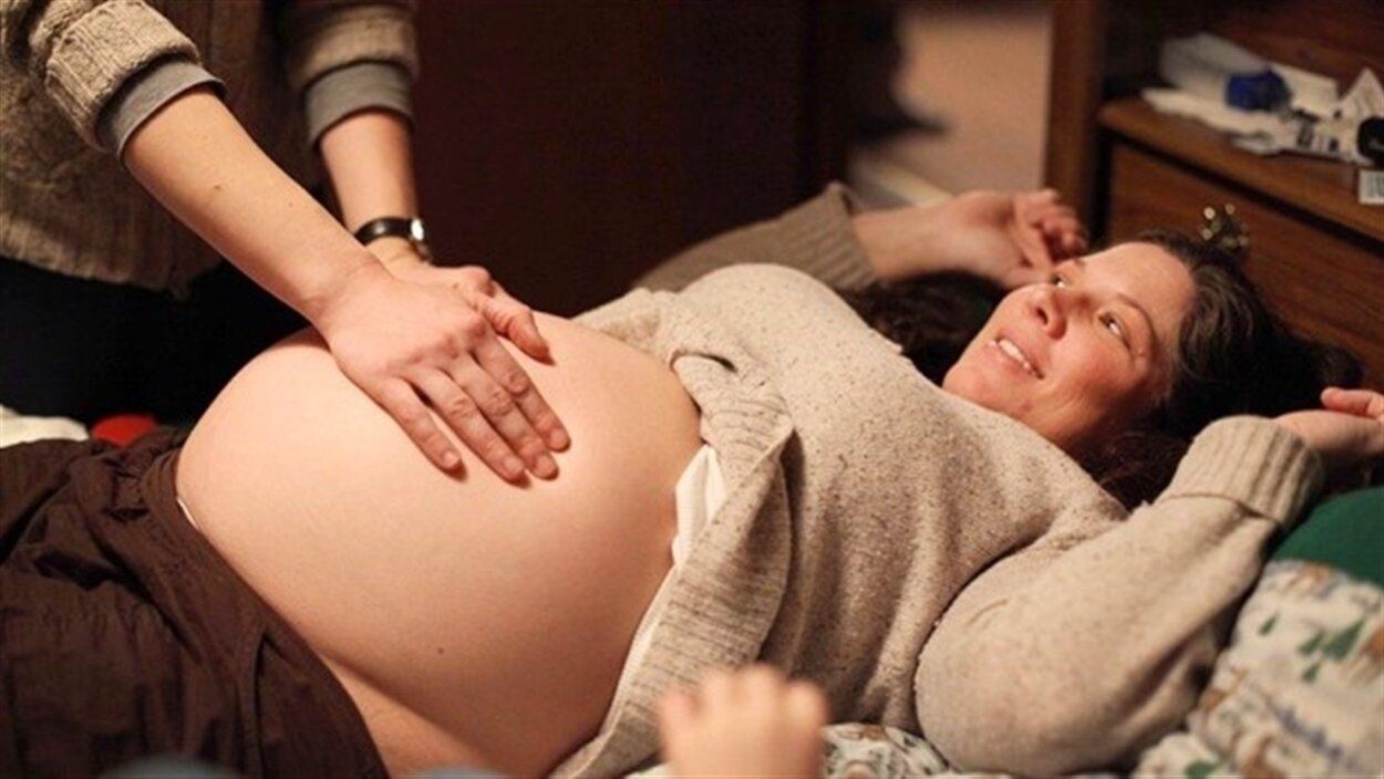 Plan moyen des mains d'une sage-femme examinant le ventre d'une femme accouchant à la maison.