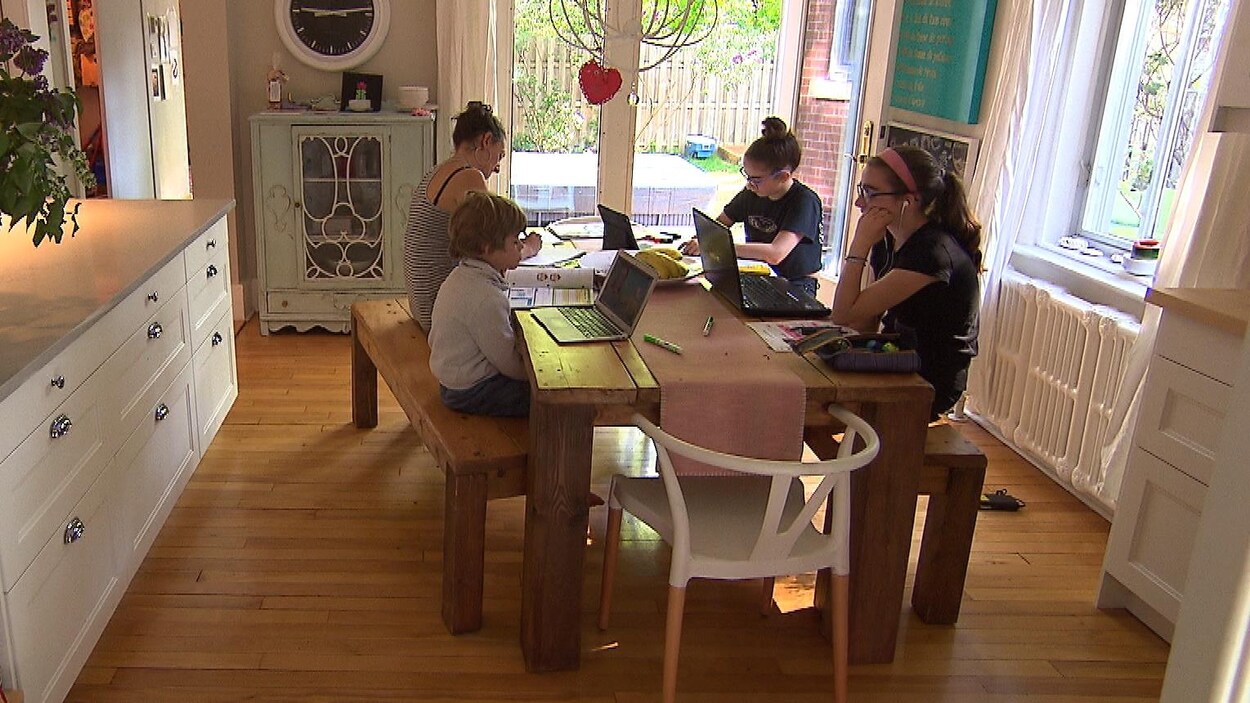 Une mère et ses trois enfants sont assis à la table de la cuisine. Ils suivent tous des cours à distance.