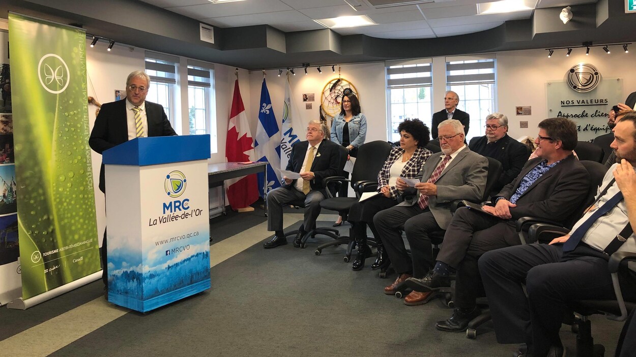 Pierre Dufour parle derrière un lutrin de la MRC de la Vallée-de-l'Or, des membres de Tourisme Abitibi-Témiscamingue dans l'assistance.