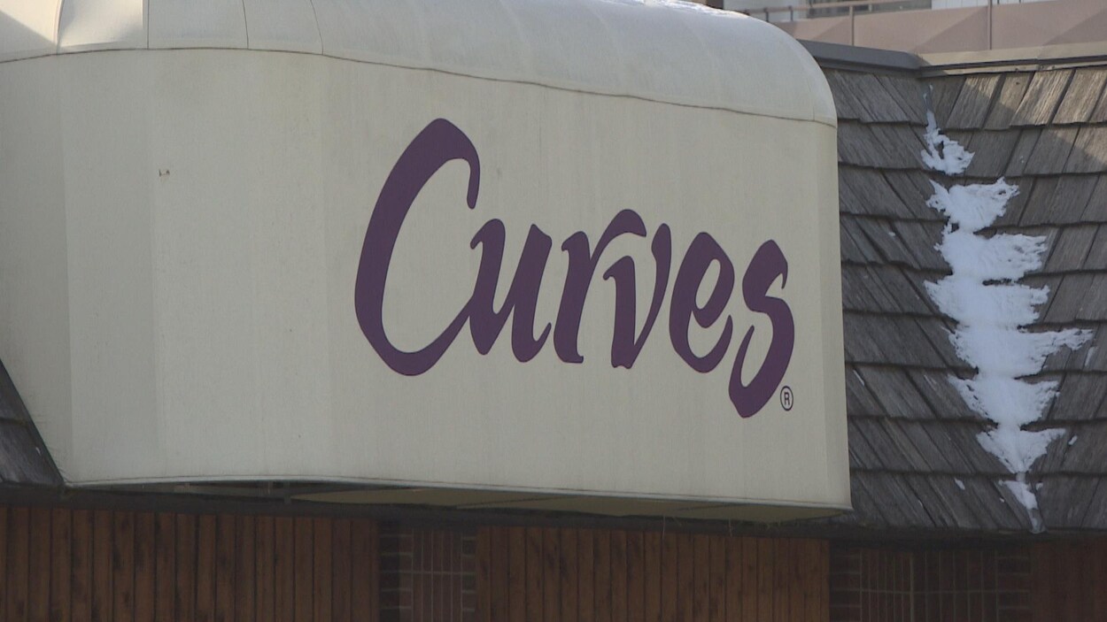 Une devanture blanche, en gros plan, sur laquelle est écrit Curves en violet. Une devanture blanche, en gros plan, sur laquelle est écrit Curves en violet.