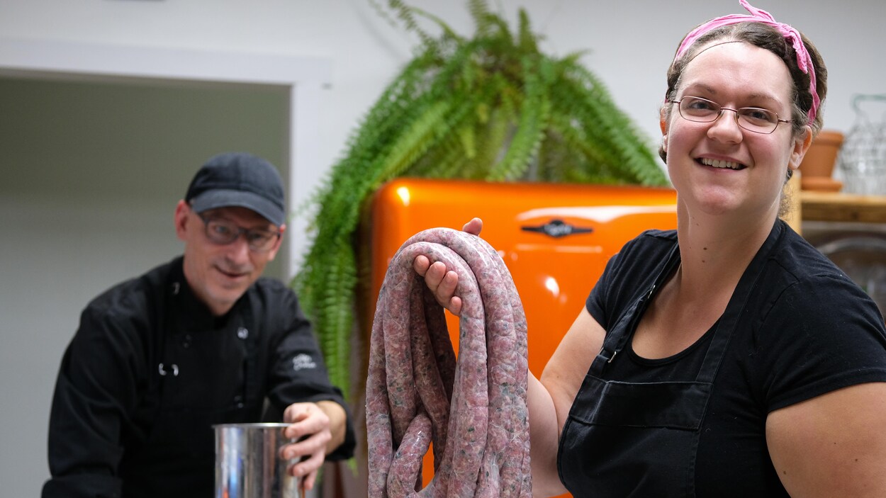 Une femme tient des saucisses dans ses mains, souriante.