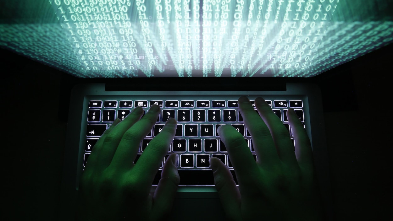 Des mains tapent sur le clavier d'un ordinateur devant un écran composé de lignes et colonnes de chiffres 1 et 0. Des mains tapent sur le clavier d'un ordinateur devant un écran composé de lignes et colonnes de chiffres 1 et 0.