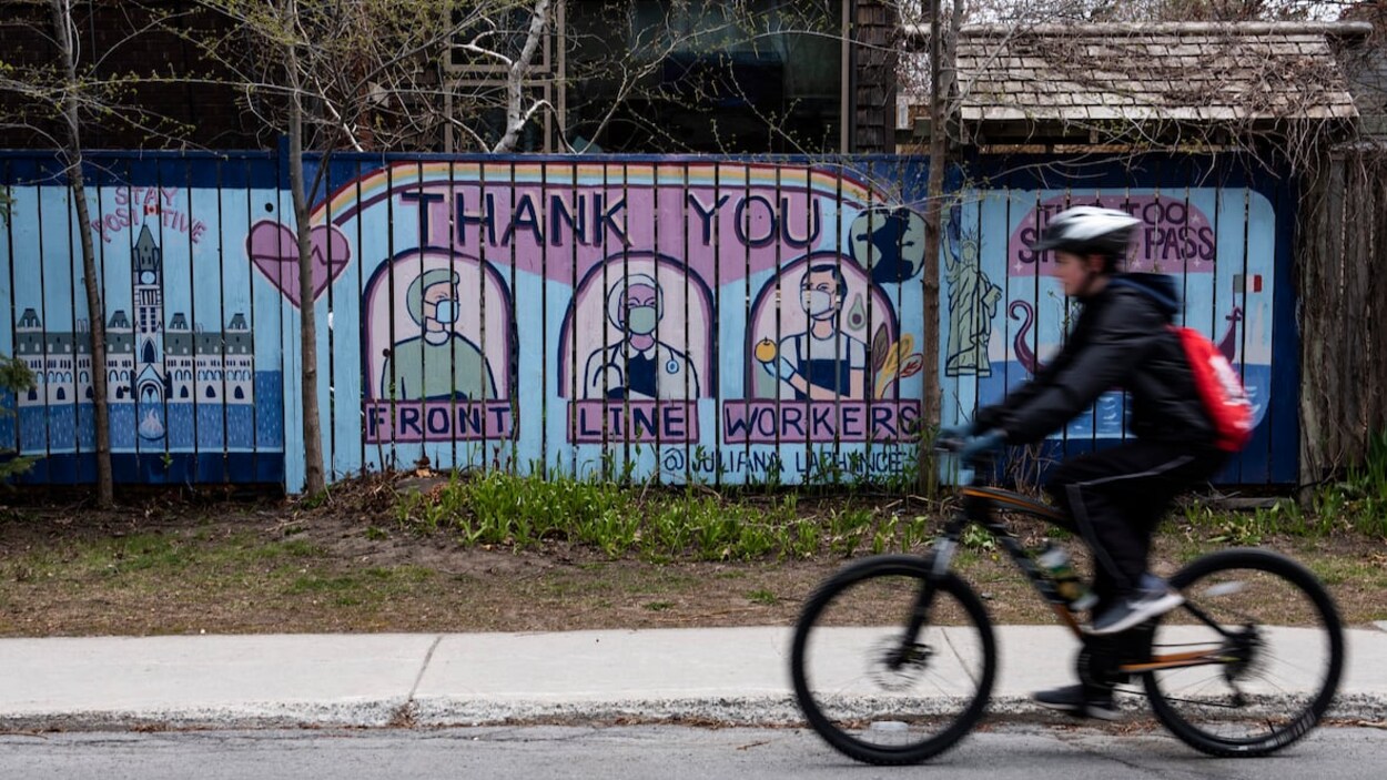 Un cycliste passe devant une murale où il est écrit : Merci aux travailleurs de première ligne.