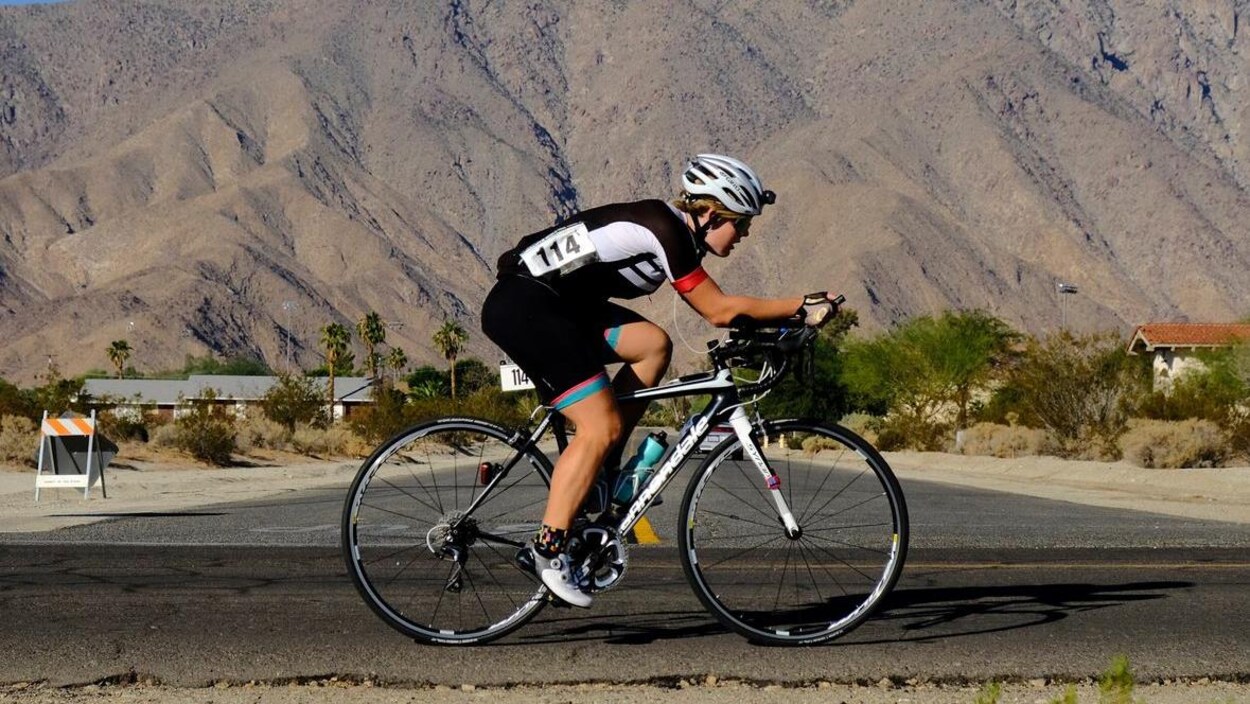 Meaghan Hackinen, à vélo dans le désert, devant une montagne et des maisons.
