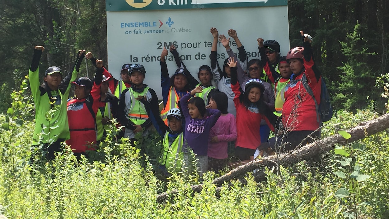 Des jeunes et des adultes autochtones lèvent les bras en l'air devant l'affiche indiquant leur arrivée à Kitcisakik.