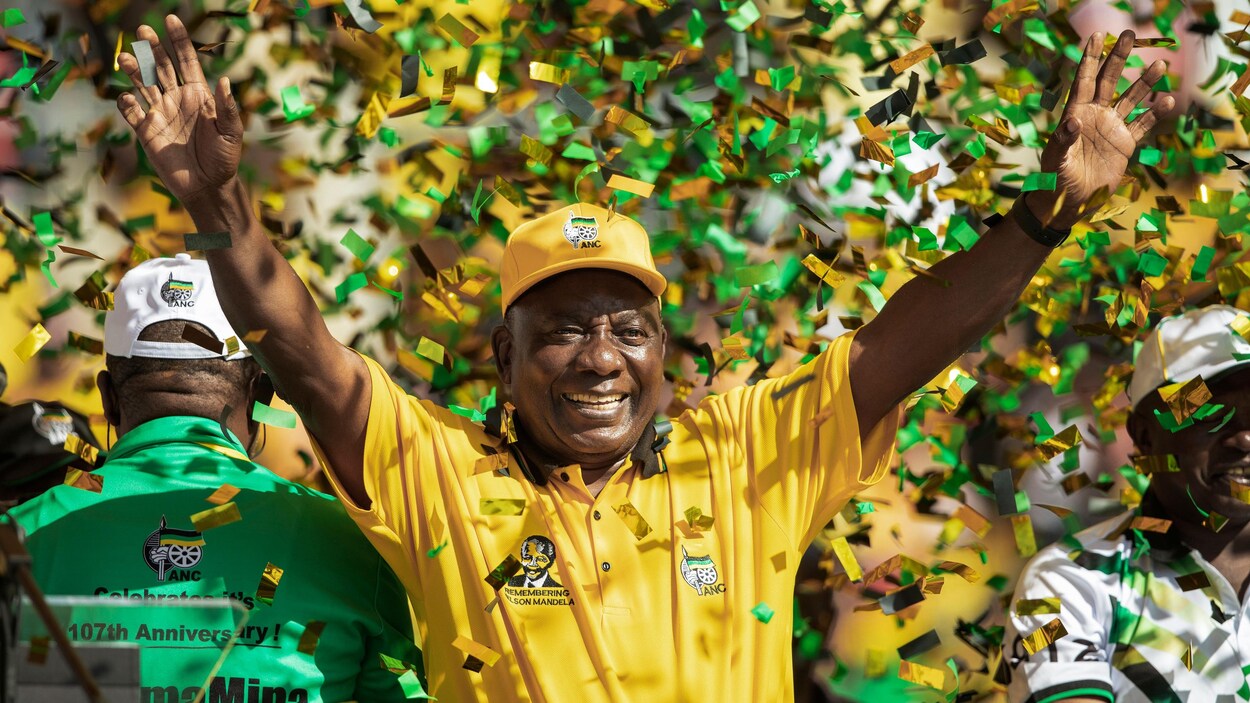 Cyril Ramaphosa, vêtu en jaune, lève les bras au ciel.