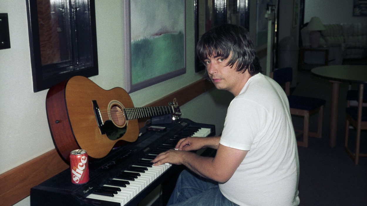 Un homme joue sur un clavier sur lequel une guitare est posée.