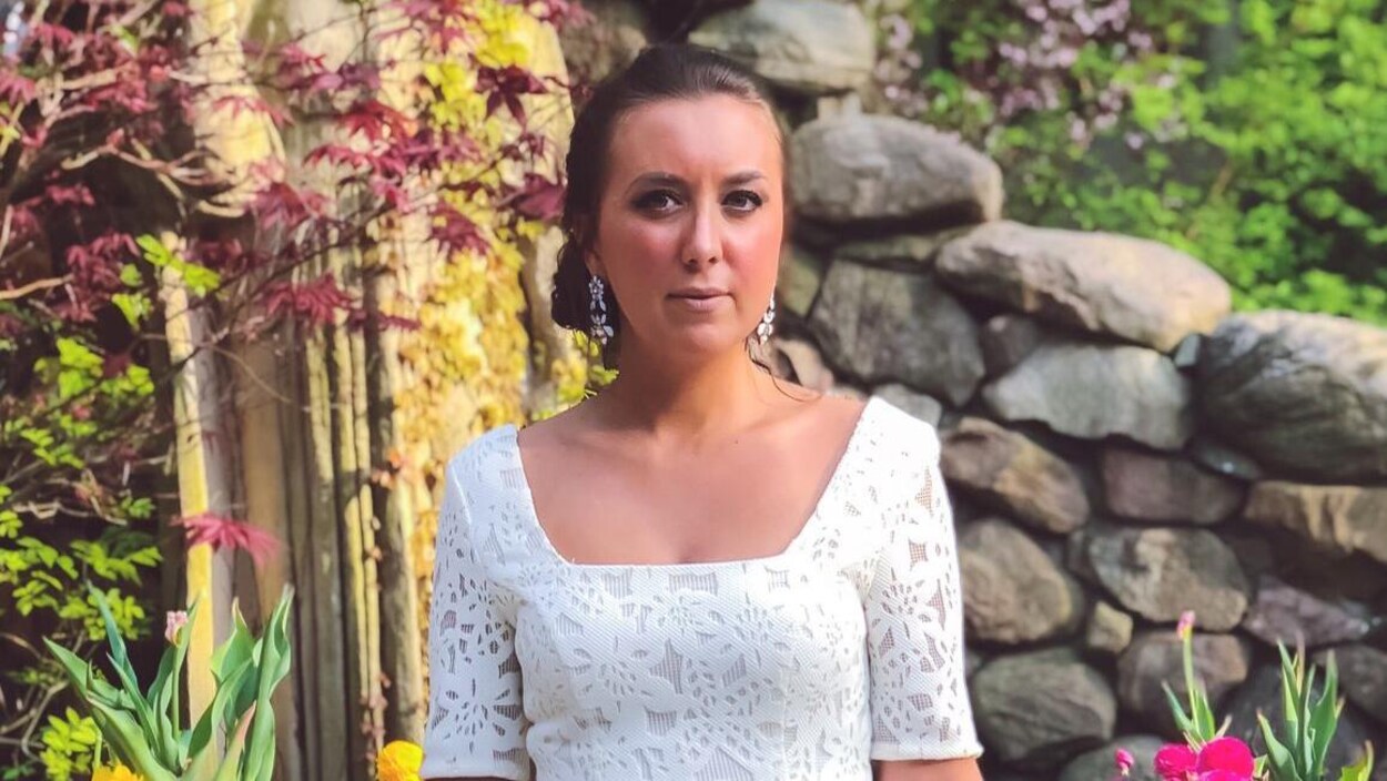 Une photo de Danielle Parent, une femme aux cheveux attachés derrière sa tête portant des boucles d'oreille blanches et une robe blanche.