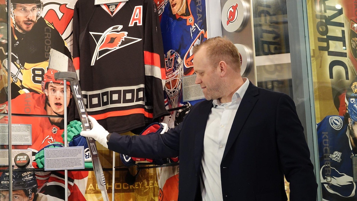 Un homme en veston devant une vitrine avec des objets de hockey.