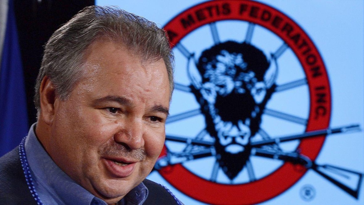 Un homme pose devant le logo de la FMM, sur lequel figurent une tête de buffle et deux carabines.