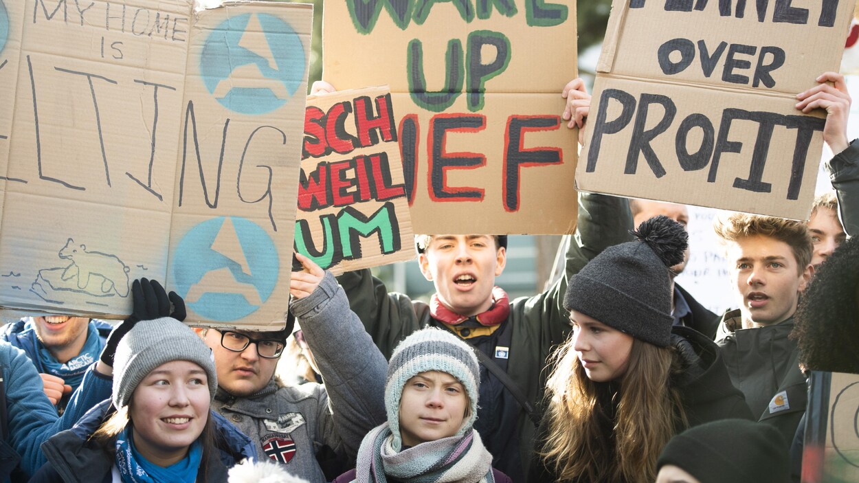 Un groupe de jeunes femmes et de jeunes hommes portant des tuques et brandissant des pancartes en faveur de l'environnement.