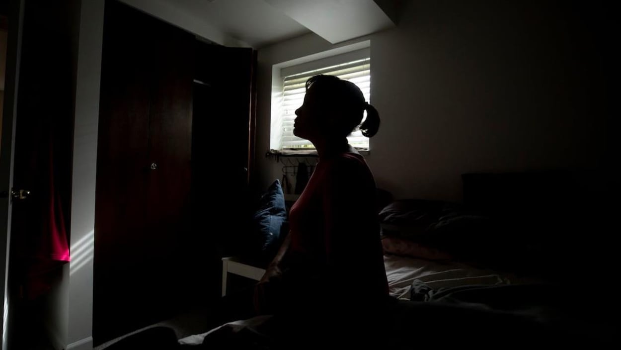 Une femme assise dans une chambre sombre.