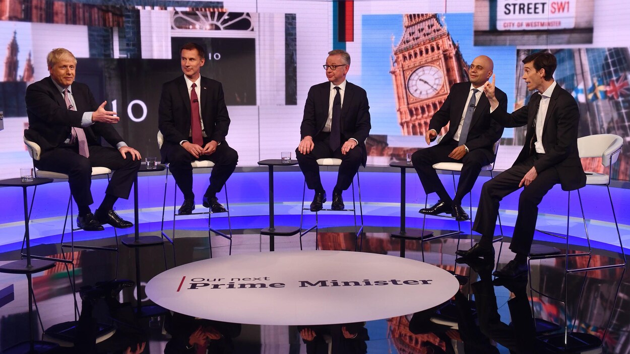 Les cinq dirigeants conservateurs sont assis sur un plateau télévisé. Rory Stewart lève son doigt et Boris Johnson a la main droite levée devant lui. Les autres candidats regardent en direction de Boris Johnson.