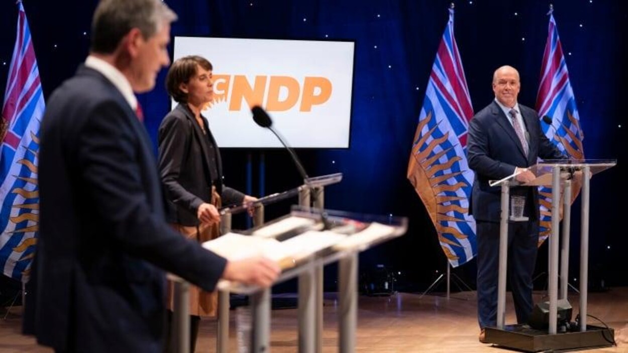 La cheffe des Verts Sonia Furstenau est debout à un lutrin au centre du chef Libéral Andrew Wilkinson et le chef du NPD John Horgan qui sont aussi tous deux à des lutrins.