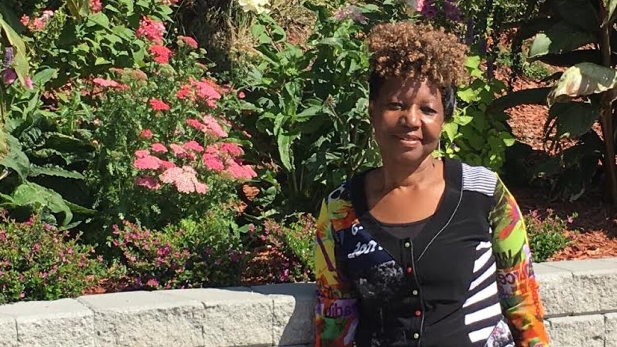 Debbie Mpofu pose pour la caméra. Elle est à l'extérieur devant des fleurs.