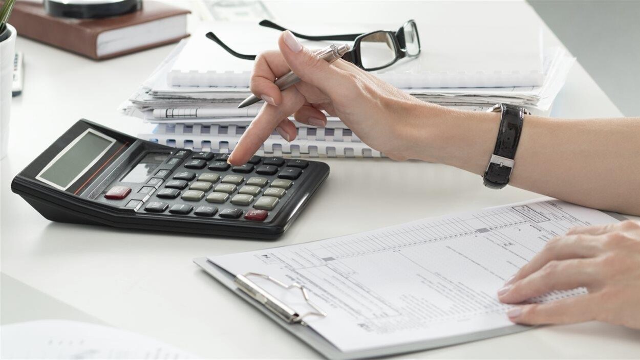Une femme remplit une déclaration de revenus à l'aide d'une calculatrice. Une femme remplit une déclaration de revenus à l'aide d'une calculatrice.