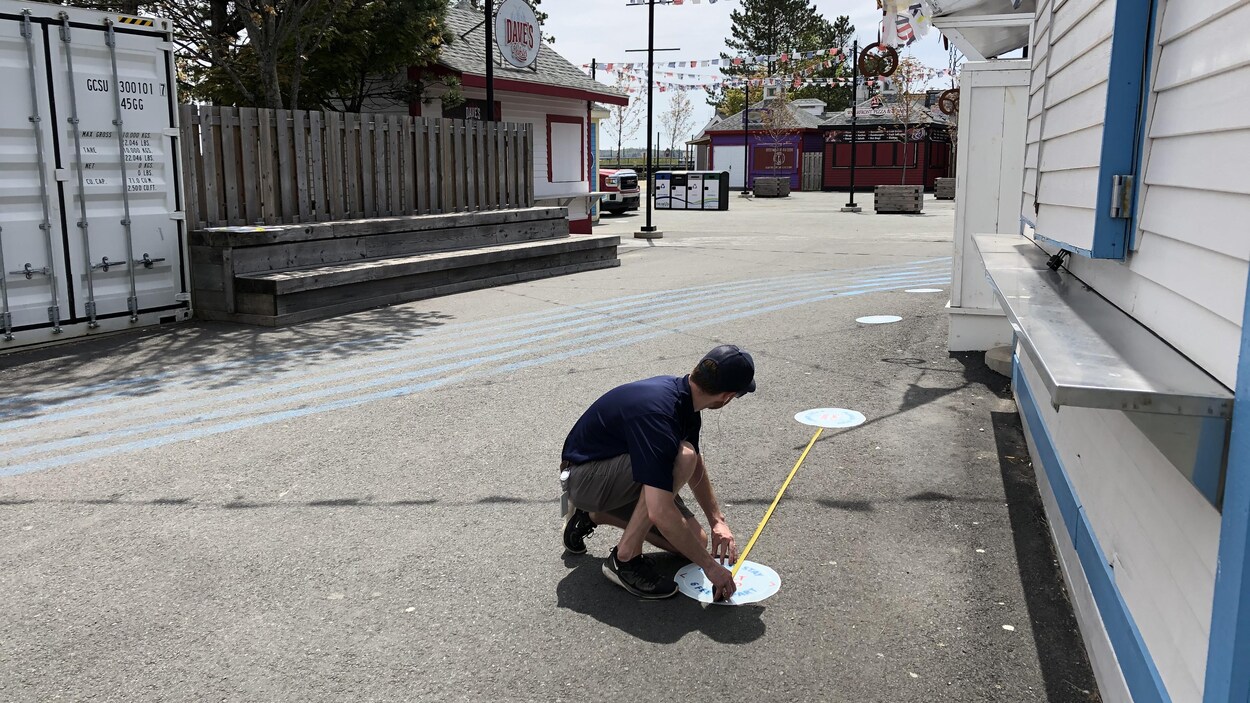 Un homme pose des autocollants sur le sol pour assurer la distanciation physique de 2 mètres.