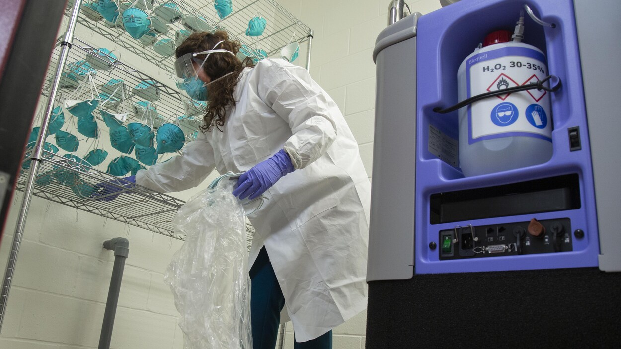 Une employée portant un masque médicale et une visière récupère des masques N-95 après une décontamination.