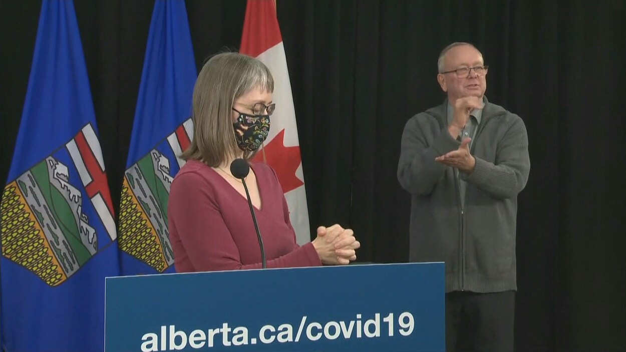 Deena Hinshaw devant son lutrin, qui se frotte les mains et porte son masque. L'interprète pour les malentendants est à sa gauche.
