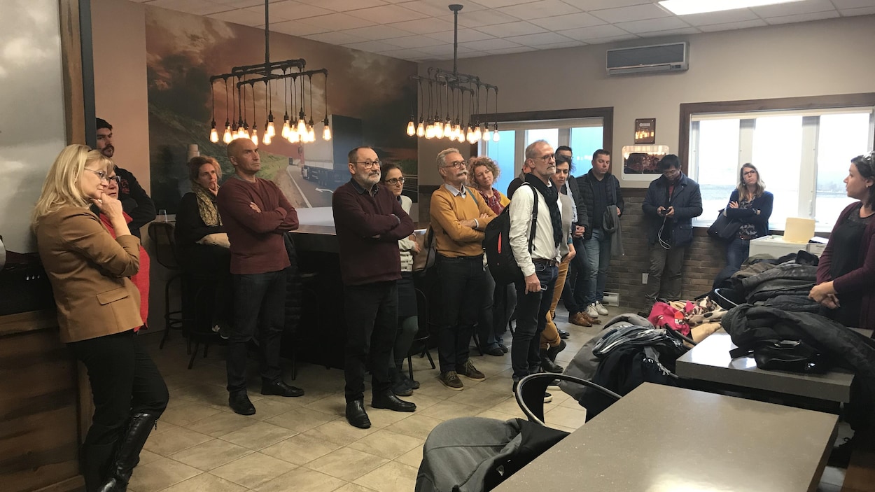 Un groupe de personnes alignées devant des tables écoutent une guide parler.