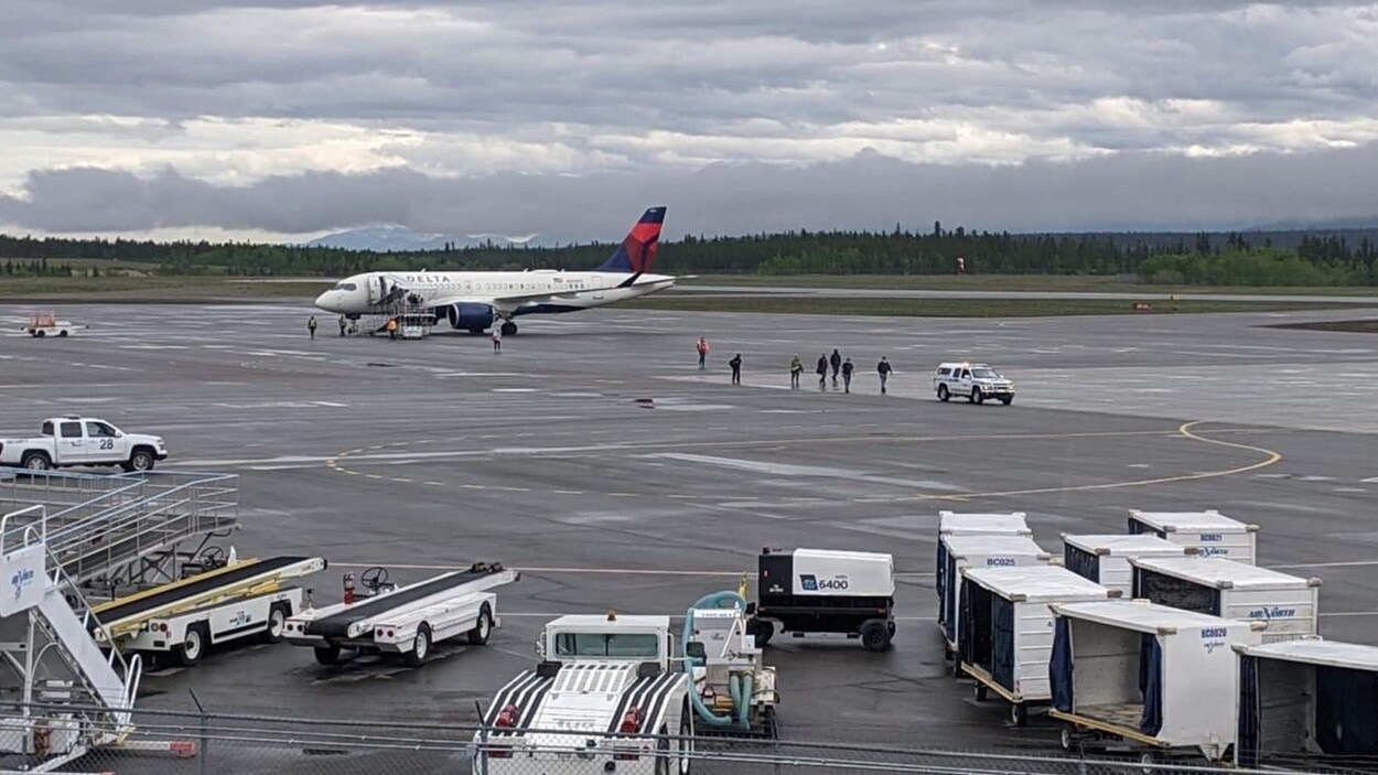 L'avion de Delta est garé sur le tarmac à Whitehorse pendant que neuf personnes se trouvent dehors sous un ciel nuageux.