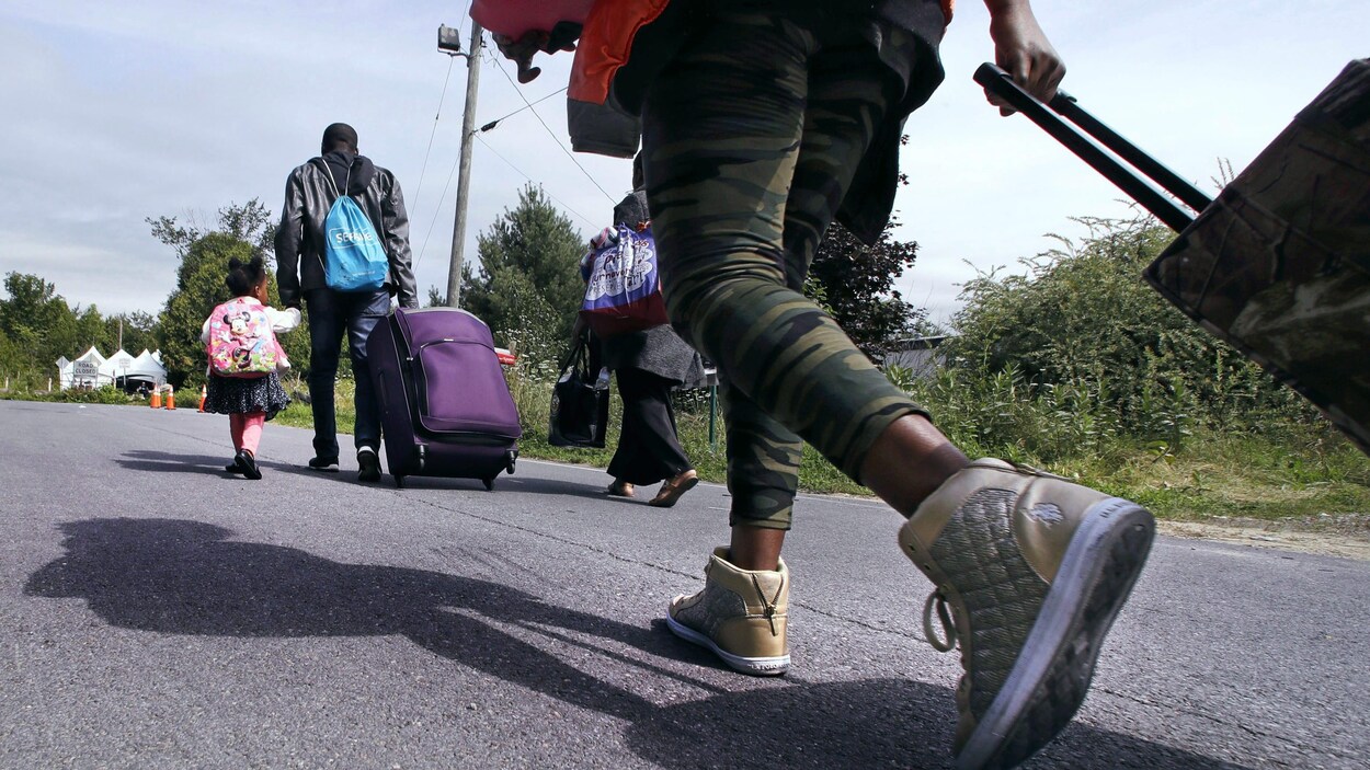 Des migrants haïtiens s'approchent de la frontière du Québec, transportant leurs valises.