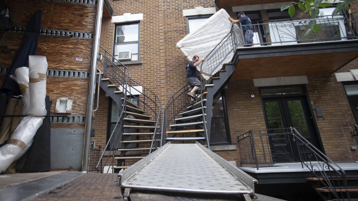 Deux déménageurs transportent un matelas dans des escaliers.