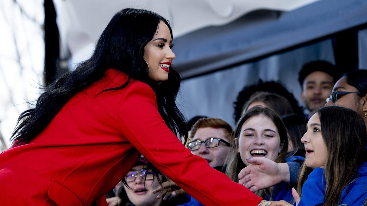 Demi Lovato, vêtue de rouge, serre la main d'adolescents qui sont tout sourire. Demi Lovato, vêtue de rouge, serre la main d'adolescents qui sont tout sourire.