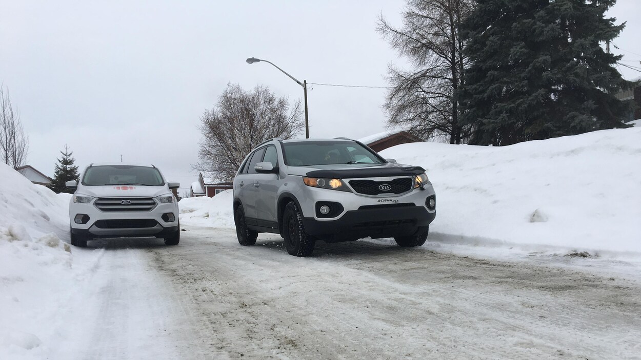 Une voiture circule dans la voie opposée pour contourner un véhicule stationné dans une rue résidentielle.