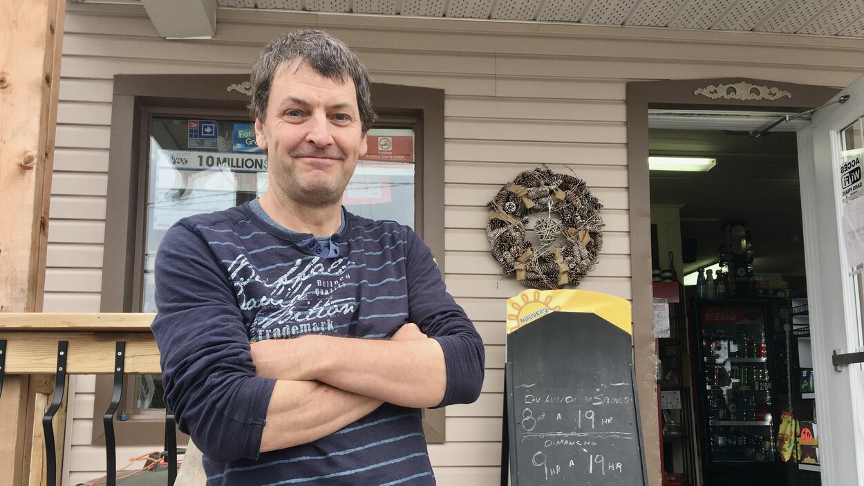 Un homme se tient devant une bâtisse avec la porte ouverte