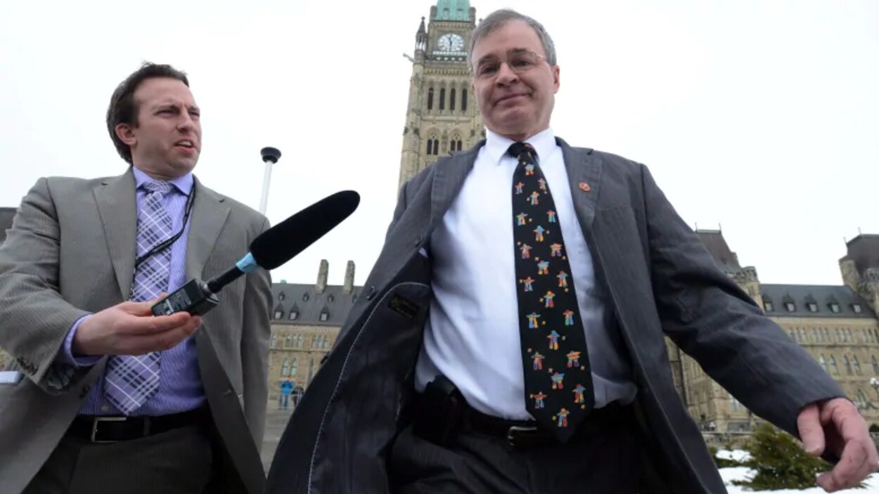 Un reporter tend un micro vers le sénateur Dennis Patterson qui marche devant le Parlement à Ottawa.