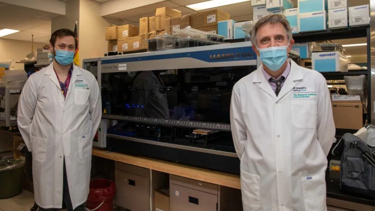 Deux hommes en sarrau et avec un masque devant de l'équipement de laboratoire.