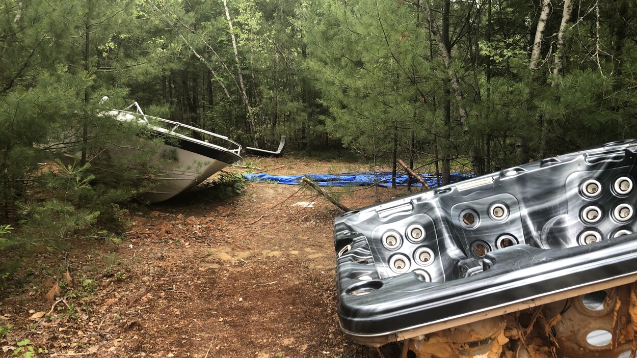 À gauche, le devant d'un bateau et à droite, la carcasse d'un spa dans un lieu boisé.