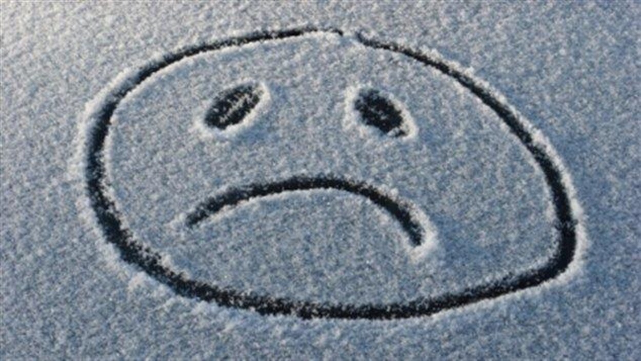 Le blues de l'hiver représenté par le dessin d'un visage triste dessiné dans la neige.