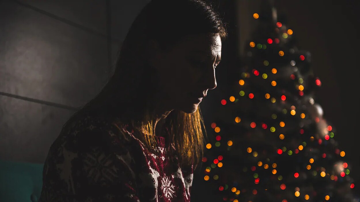 Une femme dans la pénombre avec derrière elle un arbre de Noël.