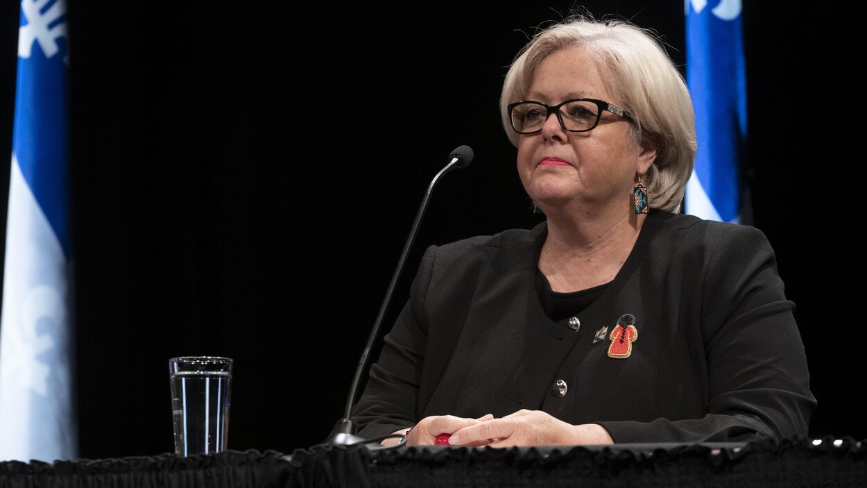 Sylvie D'Amours assise à une table devant un drapeau du Québec.