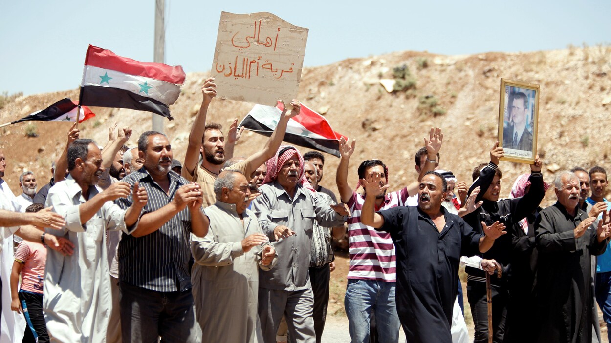 Les habitants d’Oum Al-Mayazen, banlieue de Deraa, tiennent des drapeaux syriens et le portrait du président syrien Bachar Al-Assad. Les habitants d’Oum Al-Mayazen, banlieue de Deraa, tiennent des drapeaux syriens et le portrait du président syrien Bachar Al-Assad.