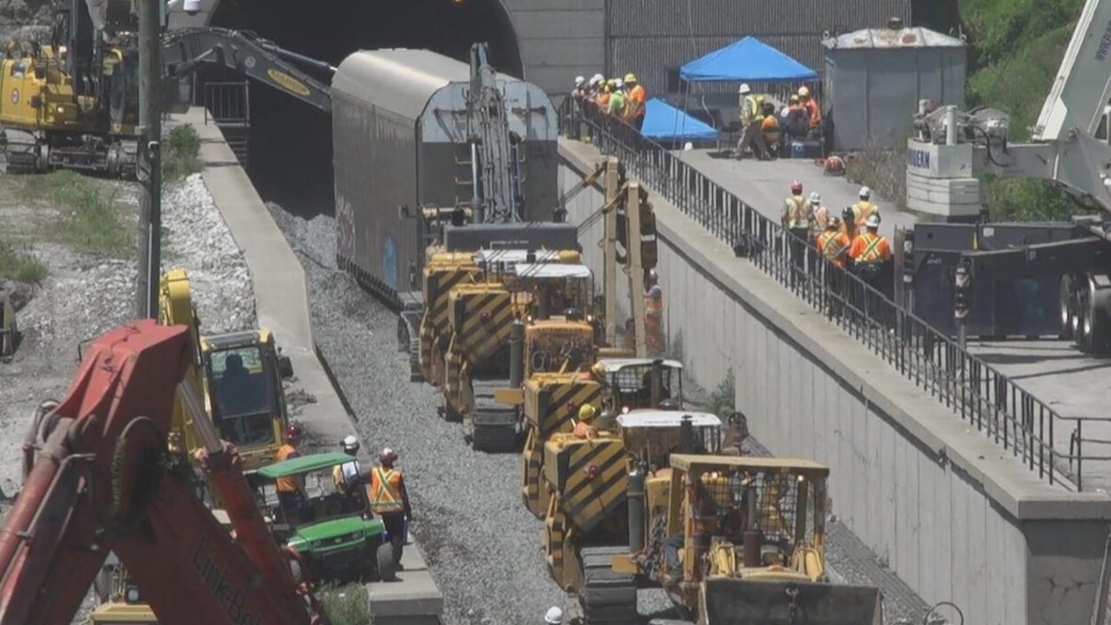 Des travailleurs s'affairent autour de matériel de chantier à l'entrée d'un tunnel.
