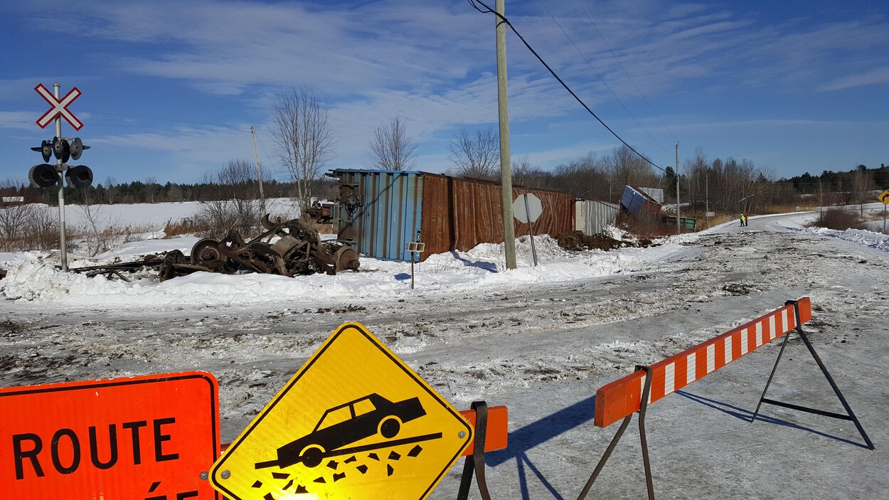 Un barrage bloque la route aux automobilistes et au loin, des wagons de train déraillés dans la neige