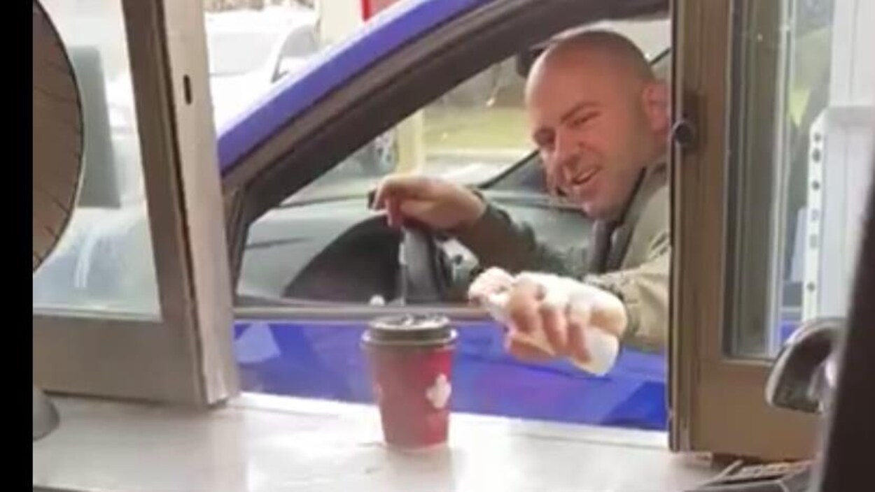Capture d'écran, un homme vaporise sa tasse de café par la fenêtre de son véhicule.