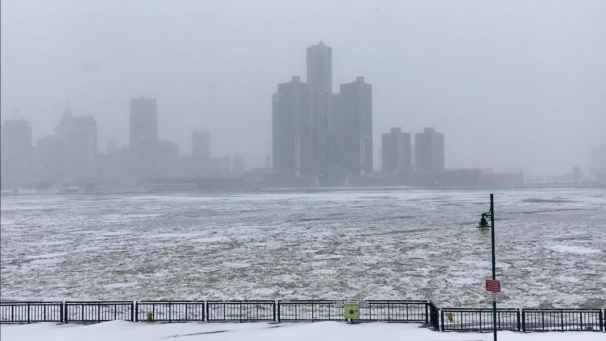 Rivière en partie glacée et centre-ville sous la neige.