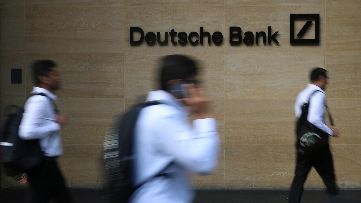Trois hommes marchent devant un mur sur lequel on voit le logo de la banque.