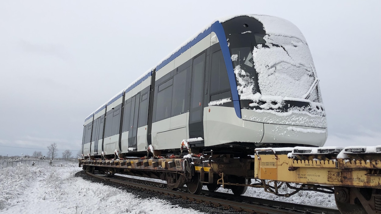 On voit le train solidement attaché sur un wagon sur rails.