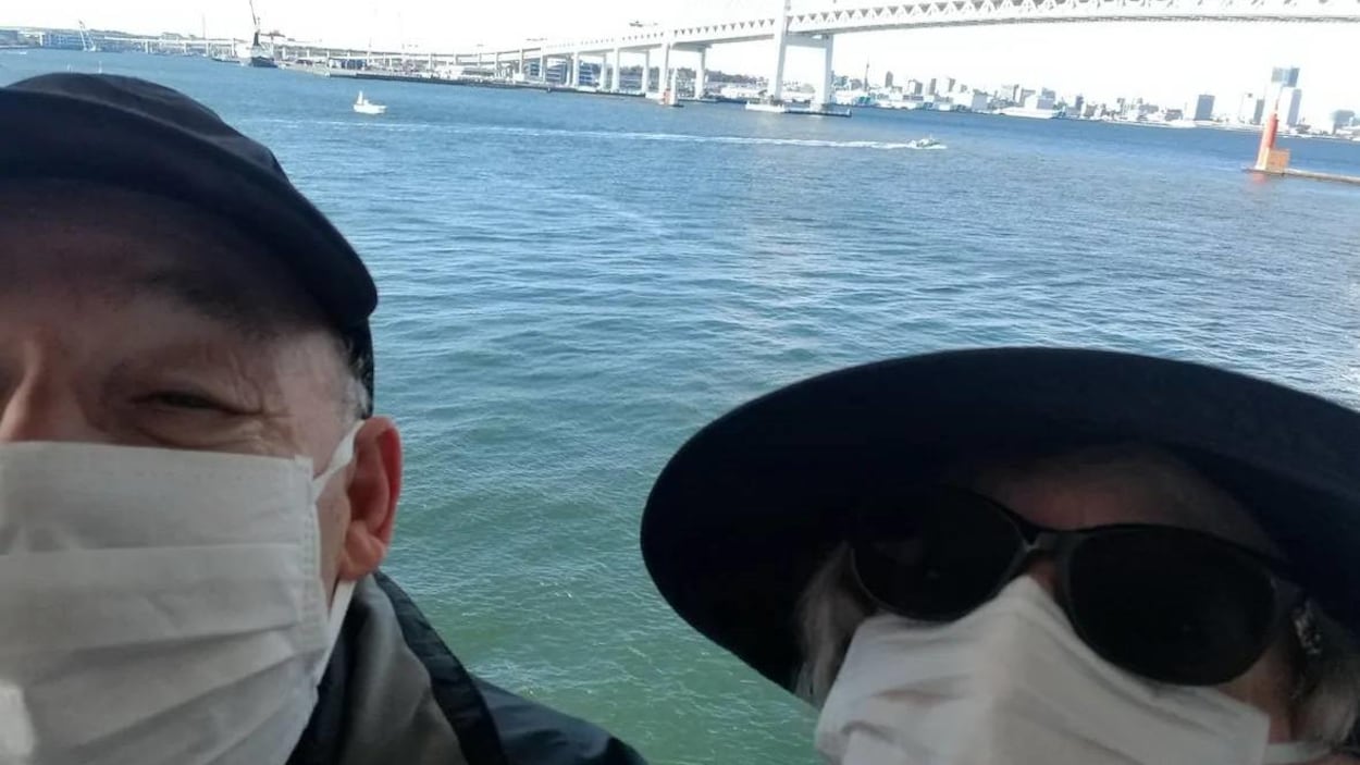 Un couple portant des masques sur la bouche et le nez se prennent en photo sur le pont d'un bateau de croisière.