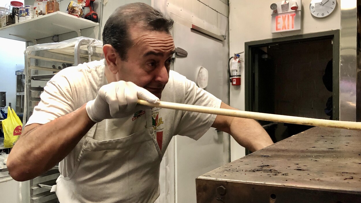 Didier, devant son four à pizza, poussant sa pelle à pizza.