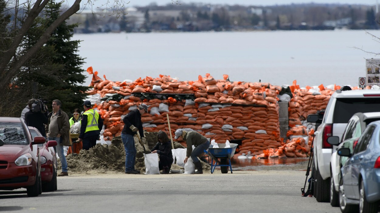 Des gens remplissent des sacs de sable, devant un mur de sacs de sable.