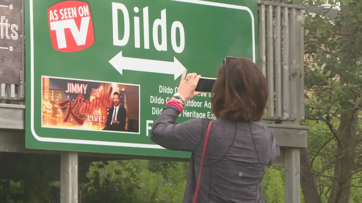 Une femme prend une photo d'une affiche indiquant le nom du village.